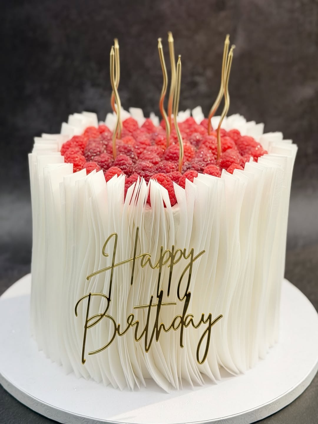 Pastel blanco con textura, frambuesas y velas doradas